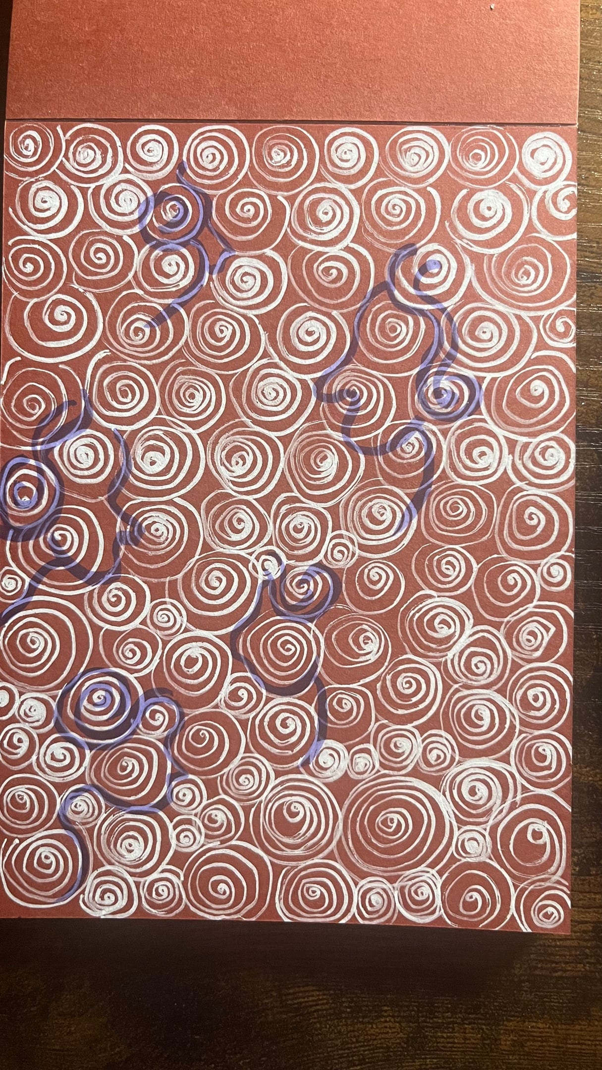 Faces in spiral ? spirals in faces, Work on paper, 2026, by Anujalika. A field of white spirals drawn on terracotta paper.